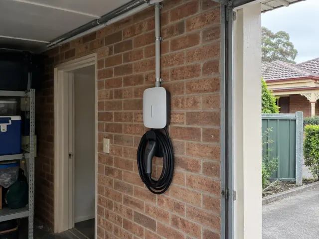 Wall-mounted EV charger on a brick garage wall with conduit and coiled cable in Wallsend
