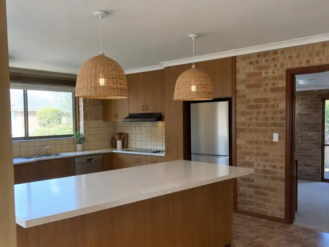 Kitchen with two woven pendant lights over a island, brick wall and timber cabinets in Rankin Park